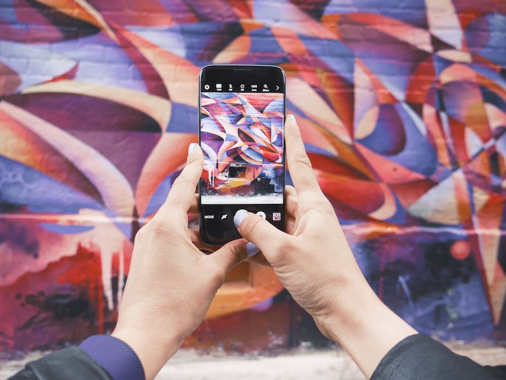 hands holding phone taking photo of wall mural